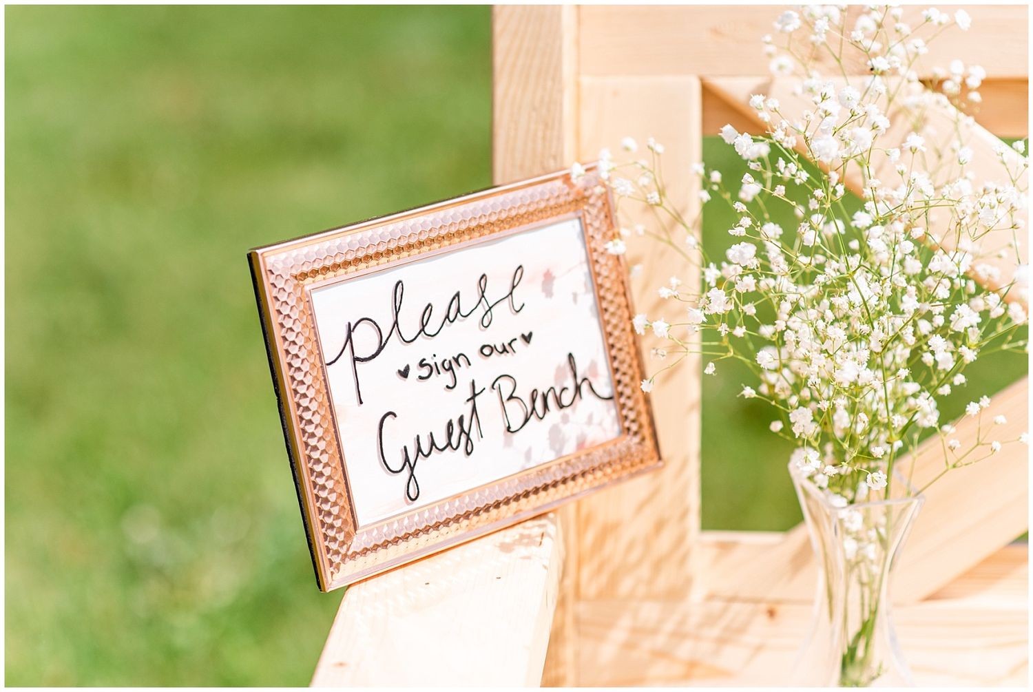 Framed sign reading please sign our guest book displayed beside baby's breath flowers at a wedding.