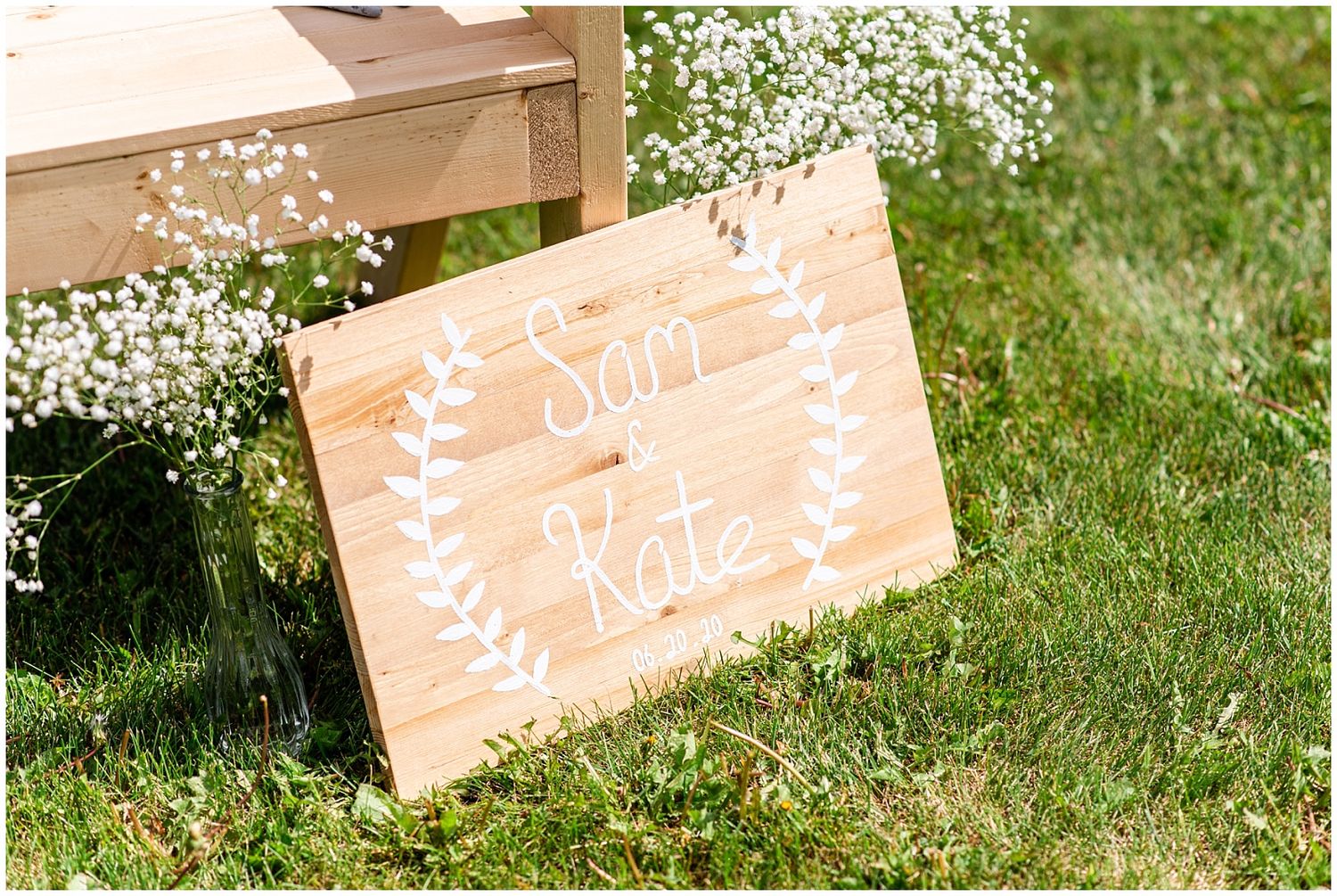 Rustic wooden wedding sign reading Sam and Kate surrounded by baby's breath flowers on green grass.