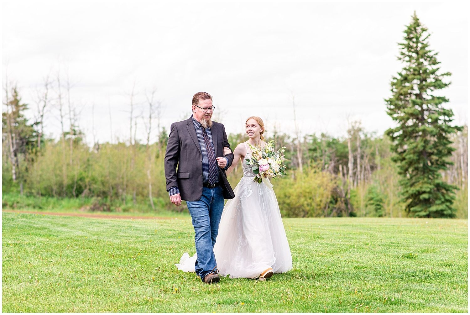 Bride and her father walking together across a green lawn at an outdoor wedding celebration.