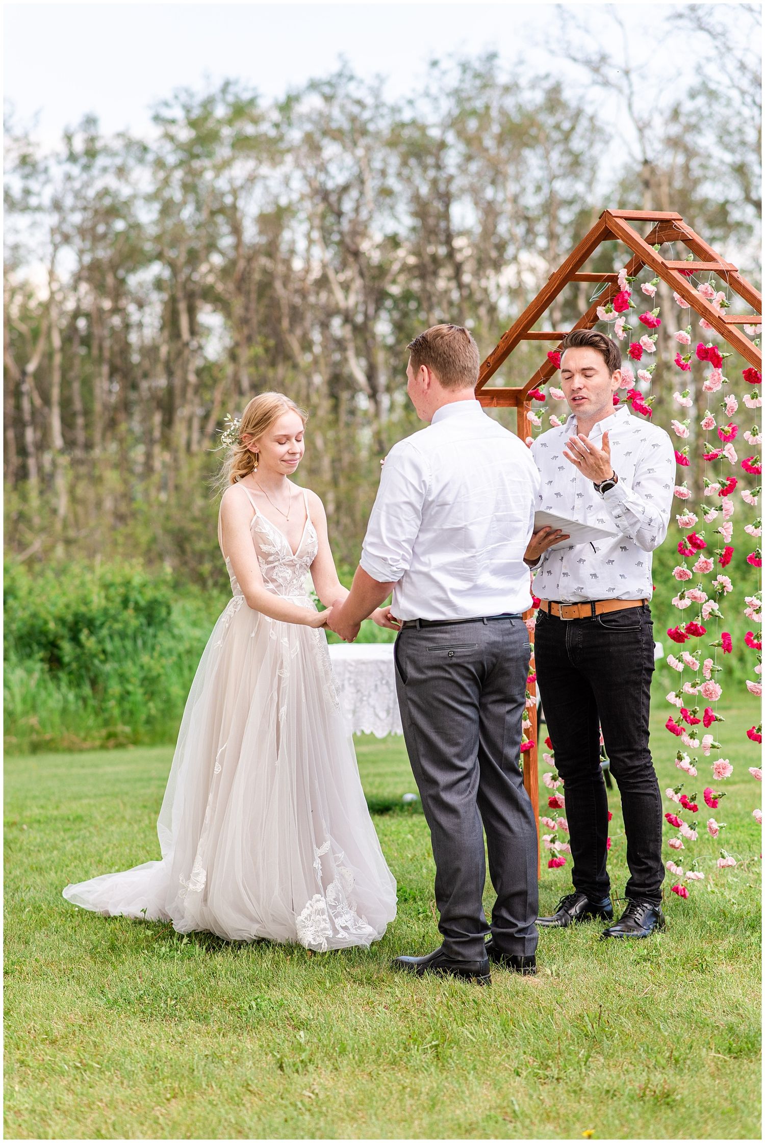 Bride and groom exchange vows outdoors at a floral arch wedding ceremony on a lush green lawn.