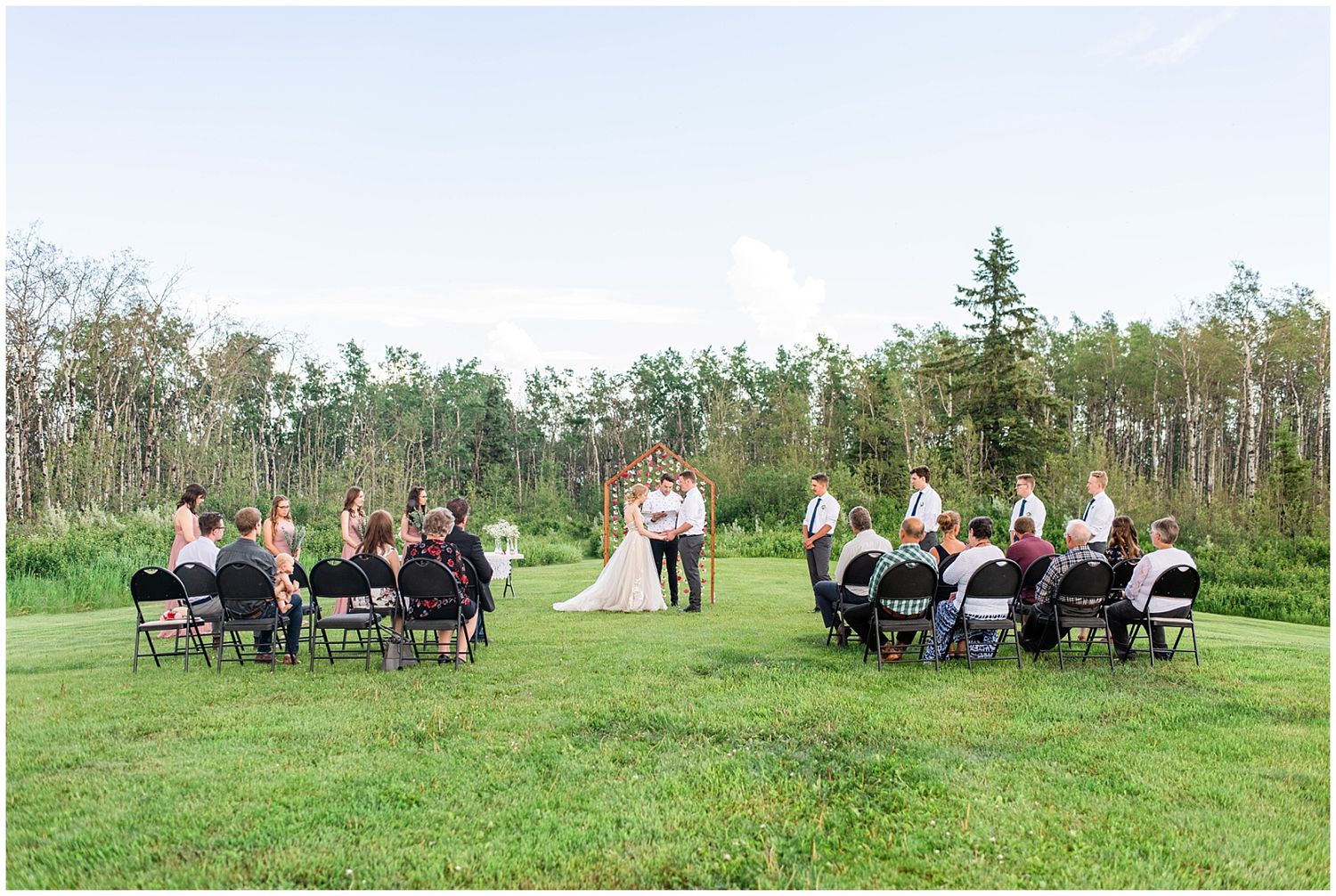 Small intimate outdoor wedding ceremony on a green lawn with guests seated in chairs facing the couple at the altar.