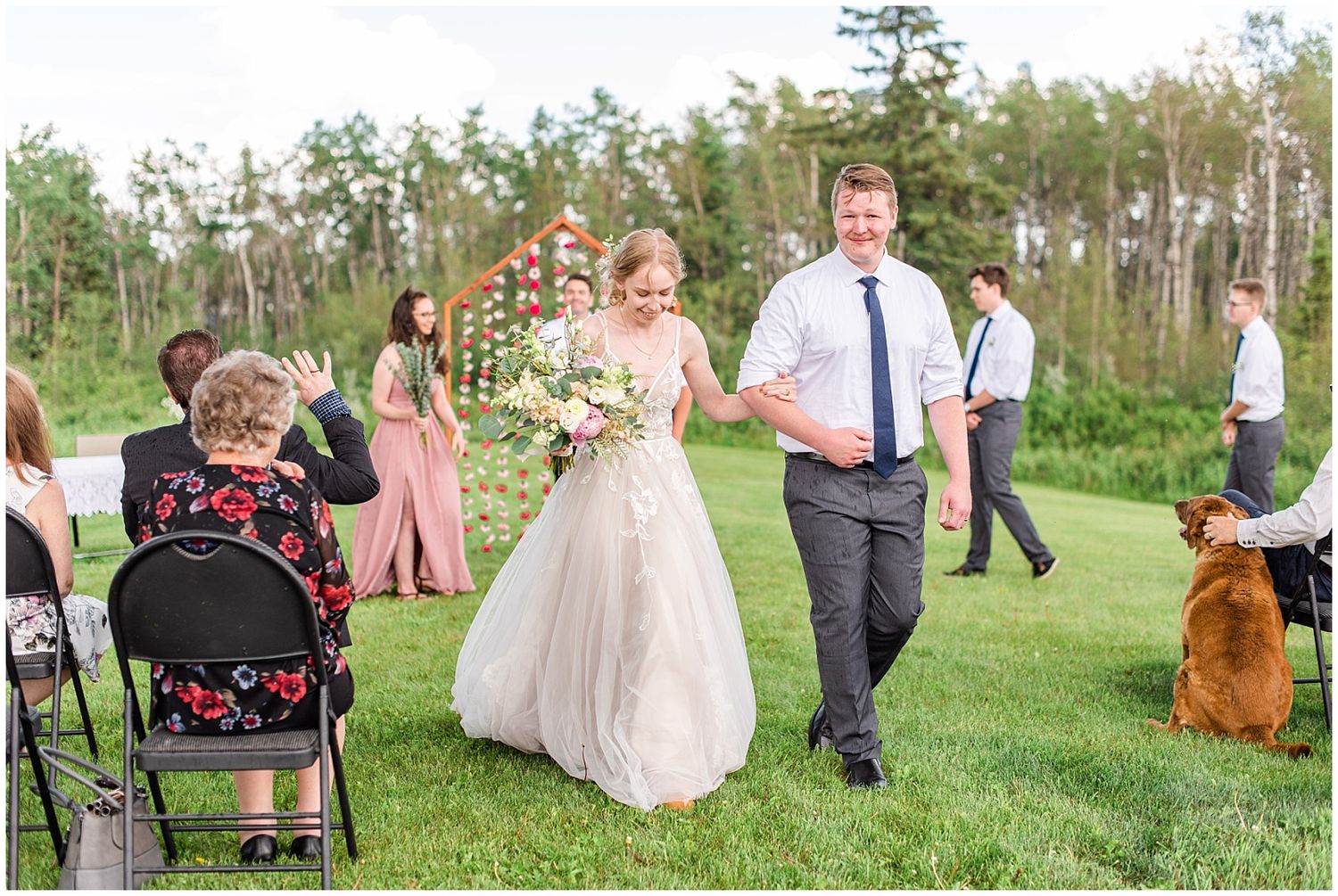 Newlyweds walk hand in hand down the aisle after outdoor wedding ceremony as guests celebrate.