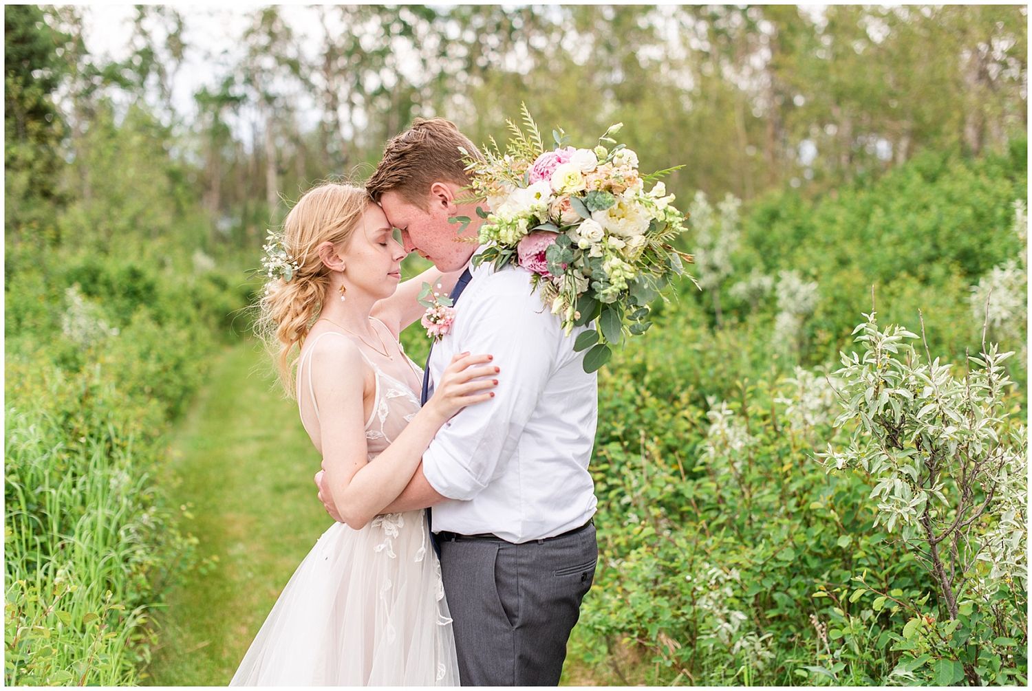 Bride and groom share a romantic moment surrounded by lush greenery, bride holding a large floral bouquet.
