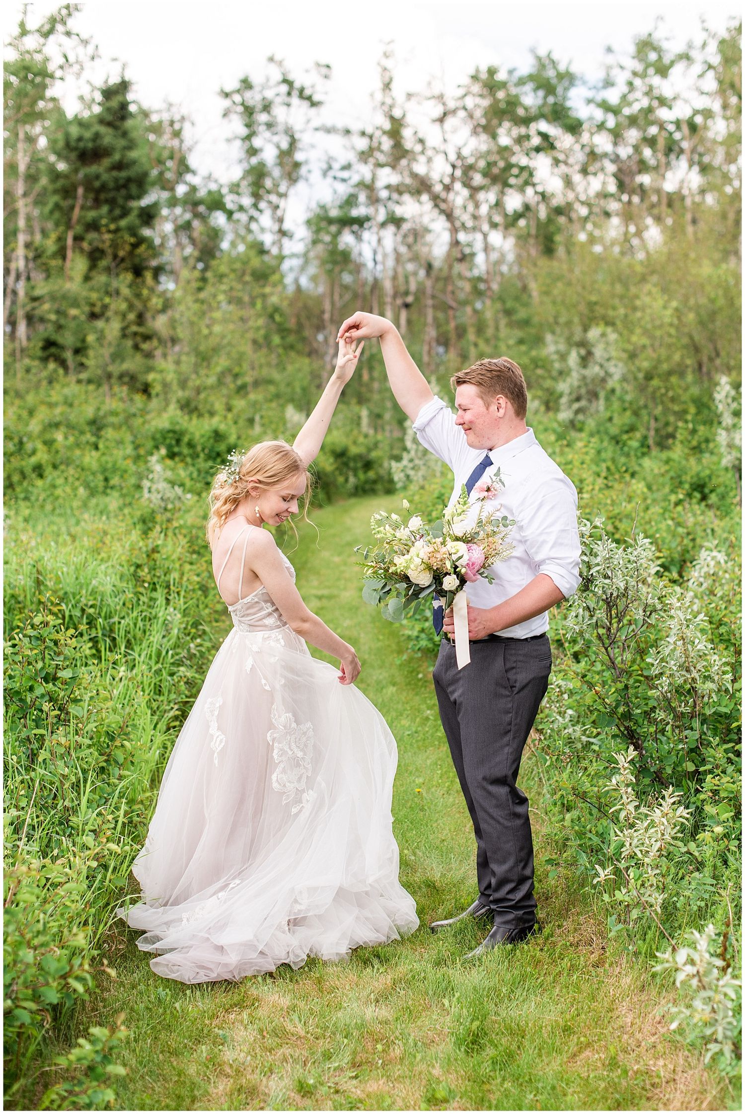 Bride and groom dancing on a lush green garden path, groom spinning bride in elegant tulle wedding gown.