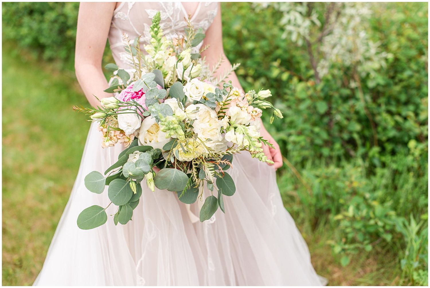 Close-up of a bridal bouquet featuring roses, eucalyptus, and mixed blooms held by a bride in a tulle gown.