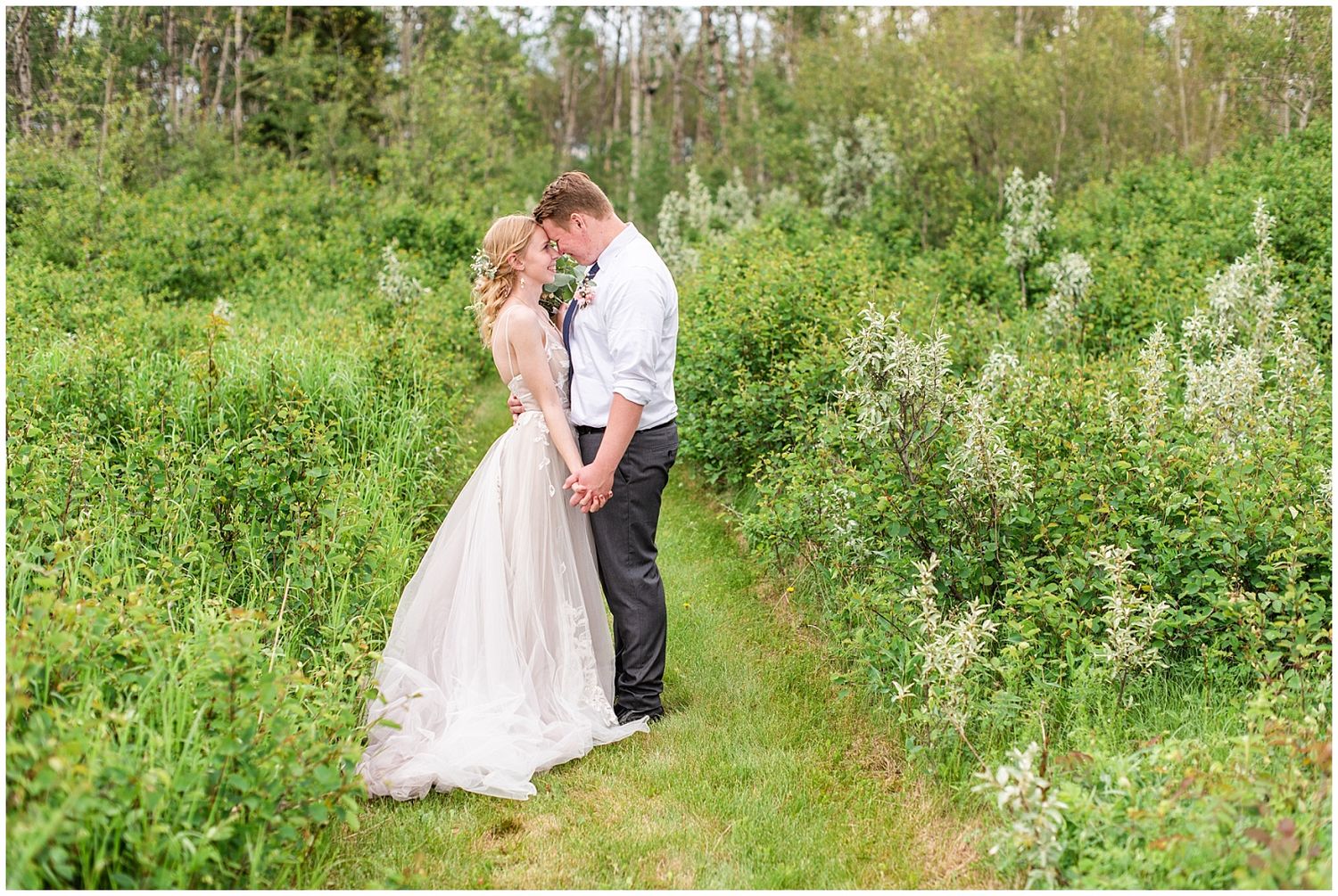 Bride and groom sharing a romantic moment on a garden path surrounded by lush green bushes.