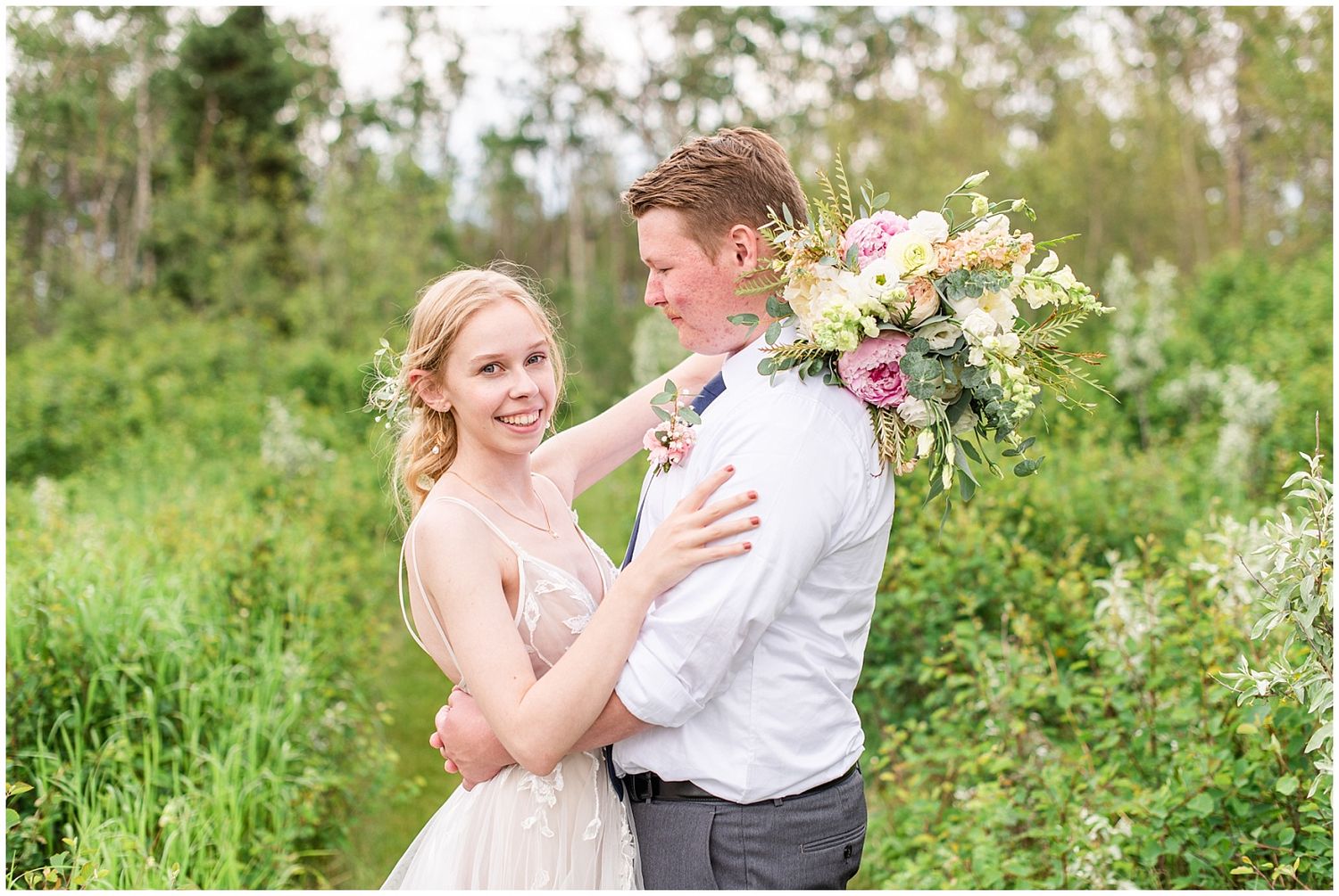 Bride embracing groom holding a colorful bouquet on a green garden path on their wedding day.