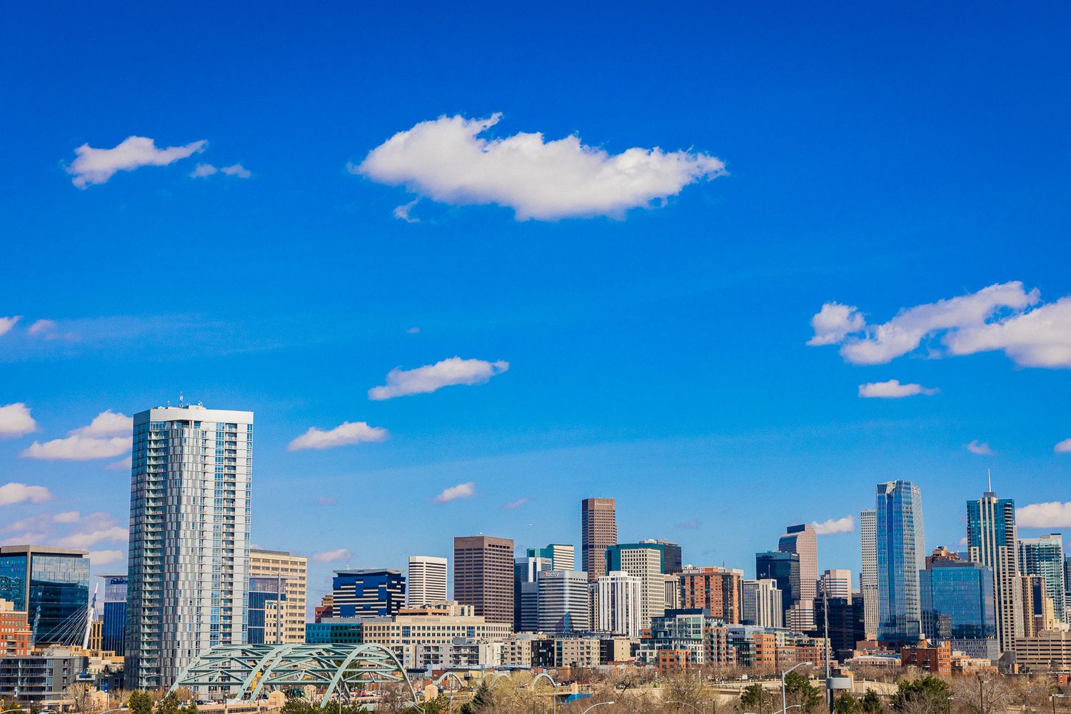 Denver city skyline with modern skyscrapers under a bright blue sky with scattered white clouds on a clear sunny day.