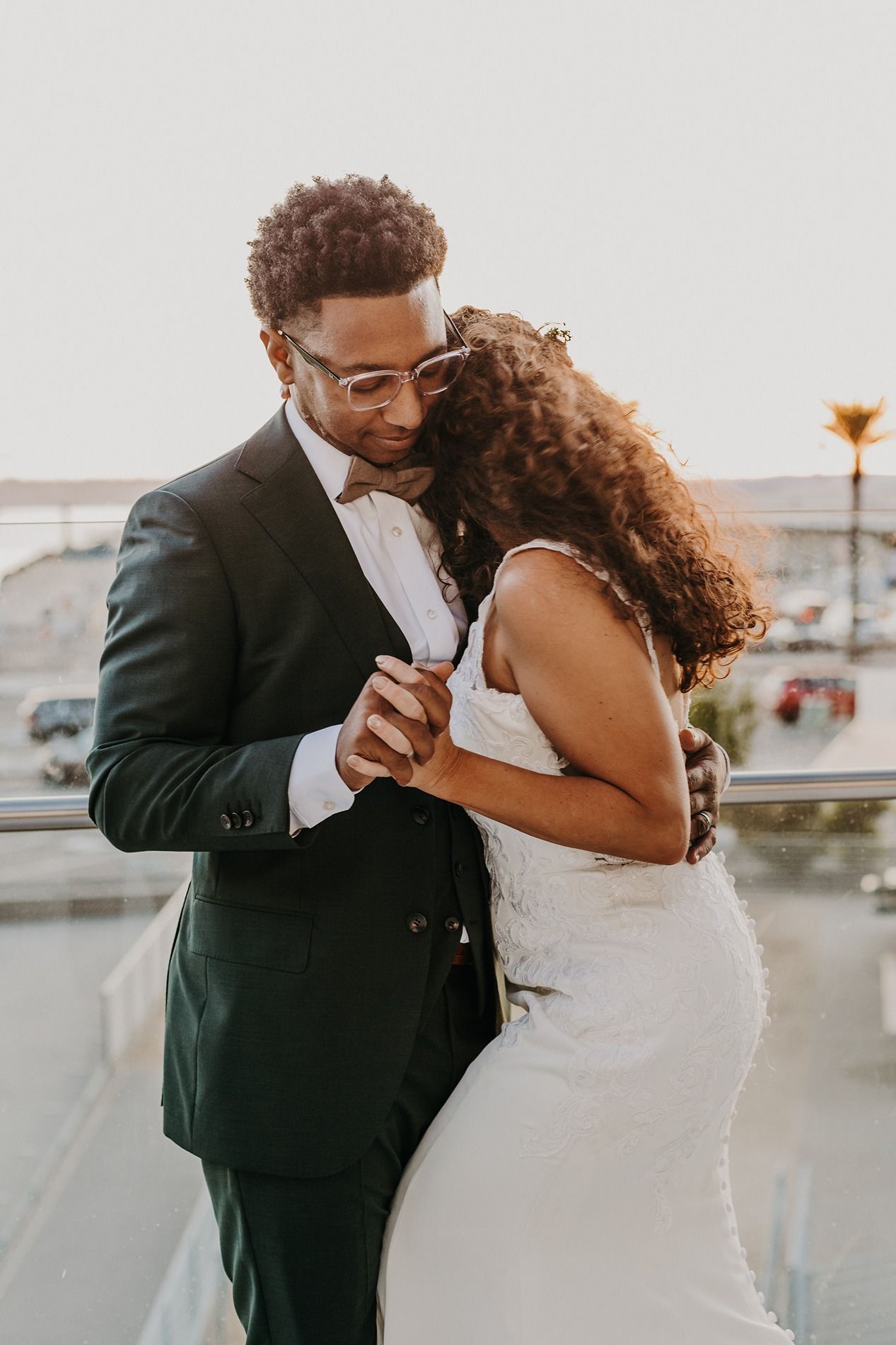 A bride and groom share a romantic embrace on a rooftop balcony, with the groom in a dark suit and the bride in a white lace gown.