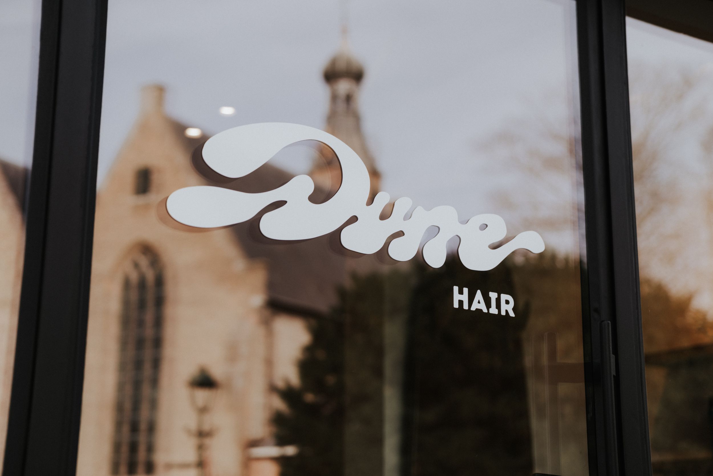 Dune Hair salon logo on a glass window with a church reflection in the background.