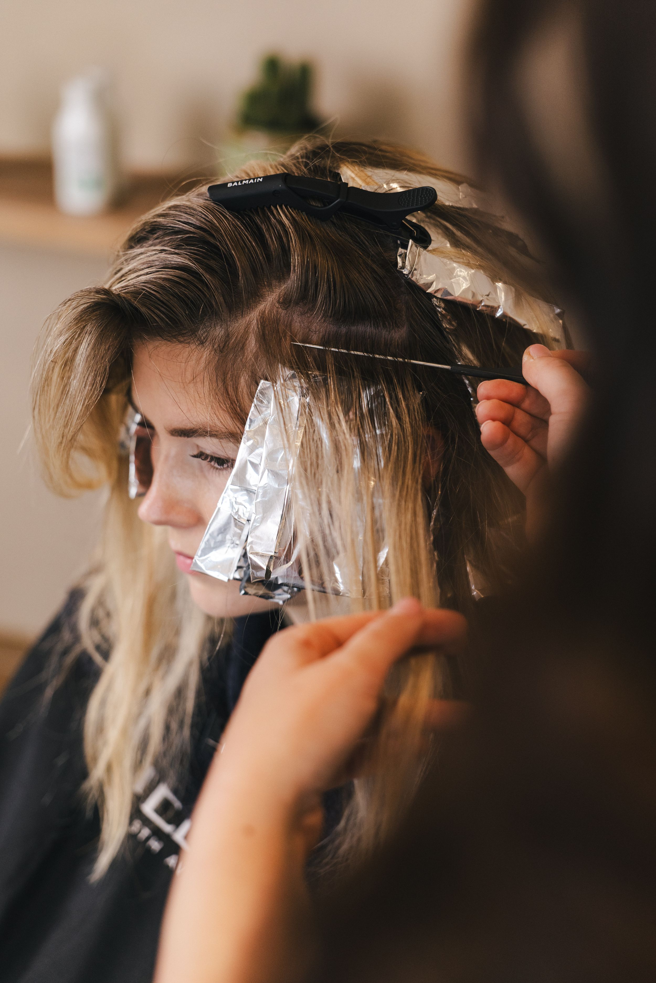 Hair colorist applying foil highlights to a blonde woman's hair in a professional salon setting.