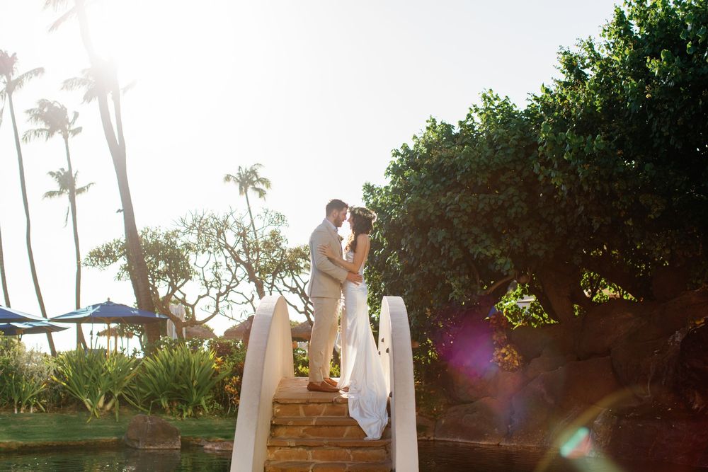 Couple sharing a romantic kiss on a sunlit stone staircase surrounded by tropical palms and lush greenery at a Hawaii wedding.