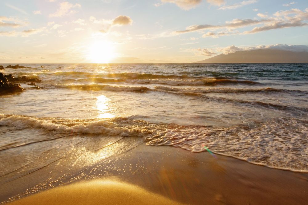 Golden sunset over calm ocean waves washing onto sandy beach with warm light reflecting on water.