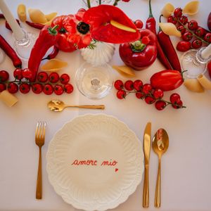 Un service de table sur le thème de l'Italie, avec une assiette « Amore mio », des couverts dorés, des légumes rouges et des pâtes.