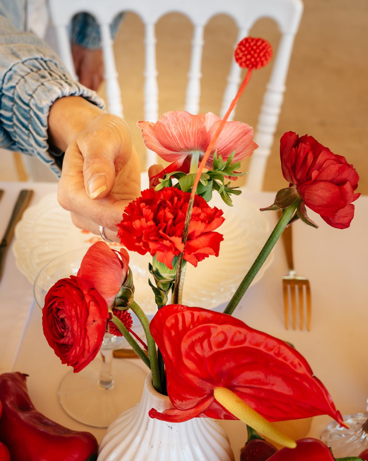 Gros plan sur une main de femme en train de positionner les fleurs sur une table de mariage. Déco rouge et blanche Dolce Vita