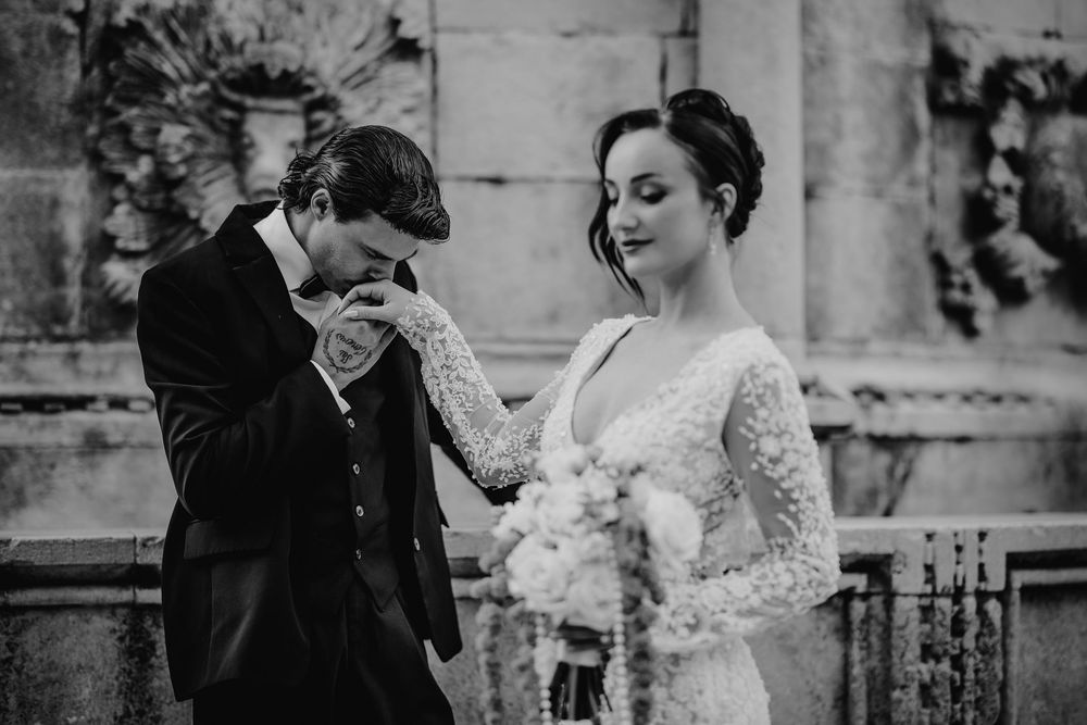 Emotional black and white wedding moment as groom kisses bride's hand lovingly.