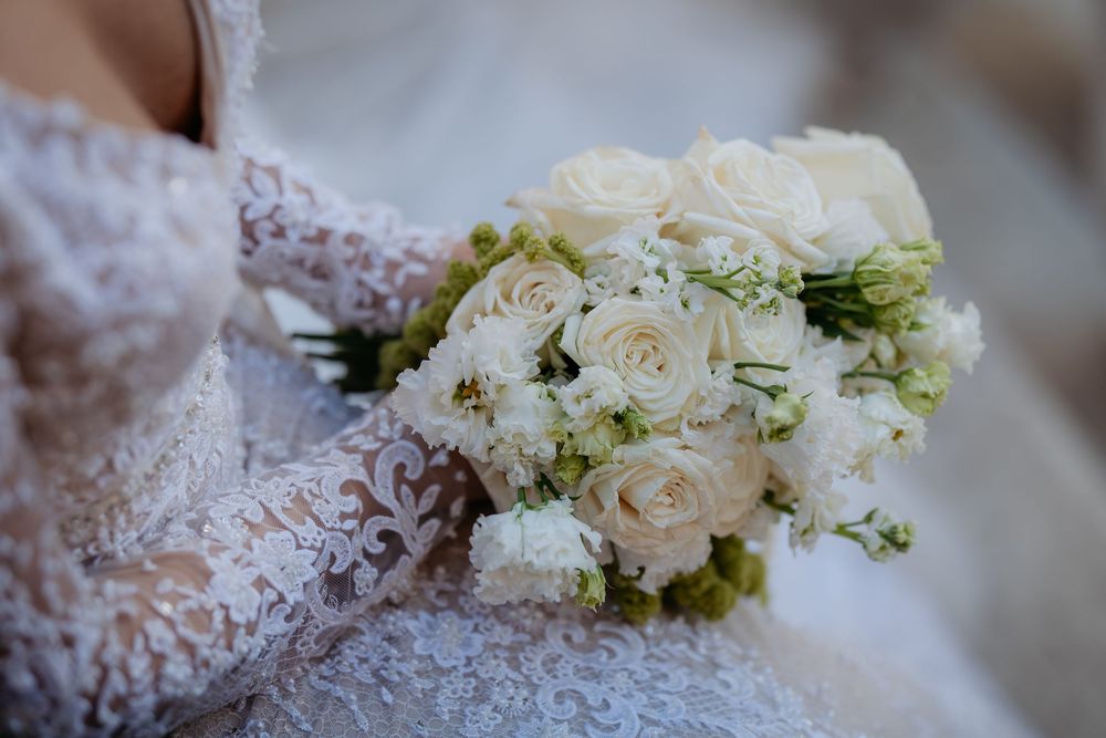Bride holding elegant white rose and peony wedding bouquet in lace dress.
