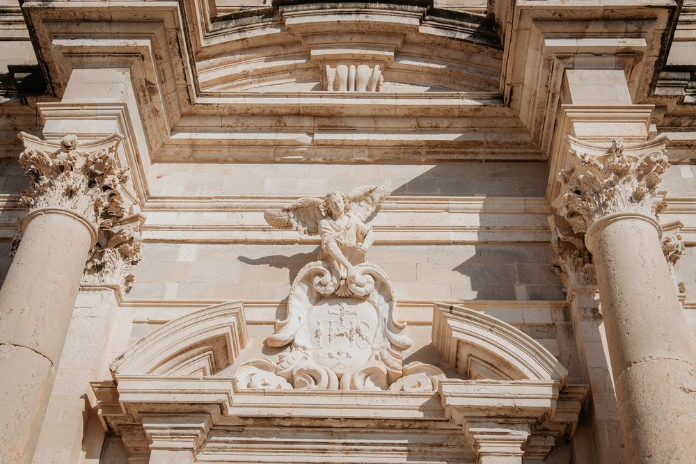Ornate Baroque church facade detail featuring carved angel sculpture between decorative stone columns.