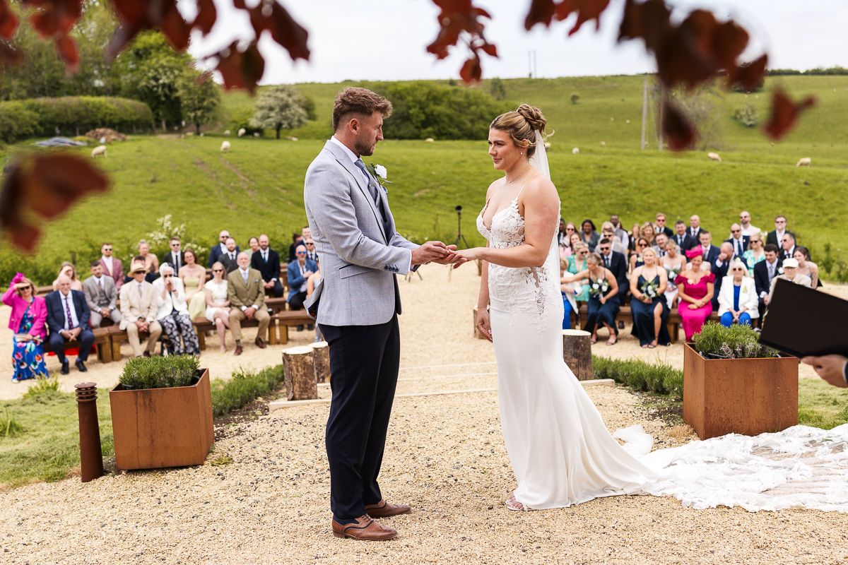 Outdoor wedding ceremony with bride and groom holding hands at rustic altar beneath a red tree.