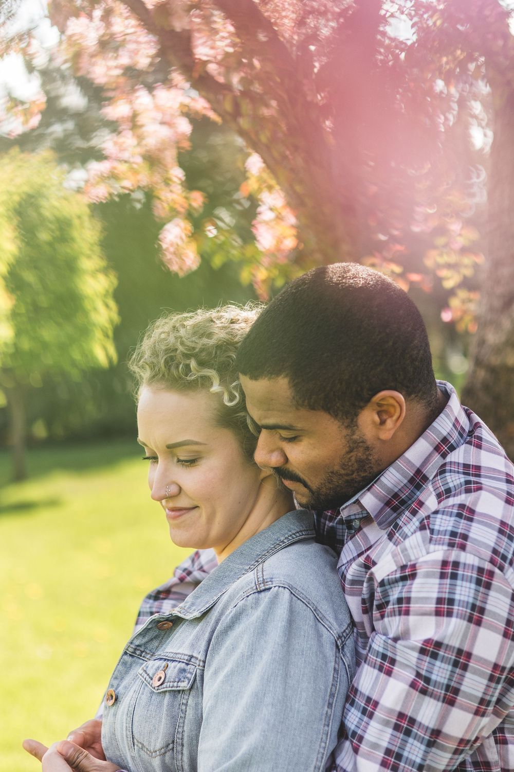 Tender moment as a man embraces a woman from behind under colorful autumn trees in sunlight.