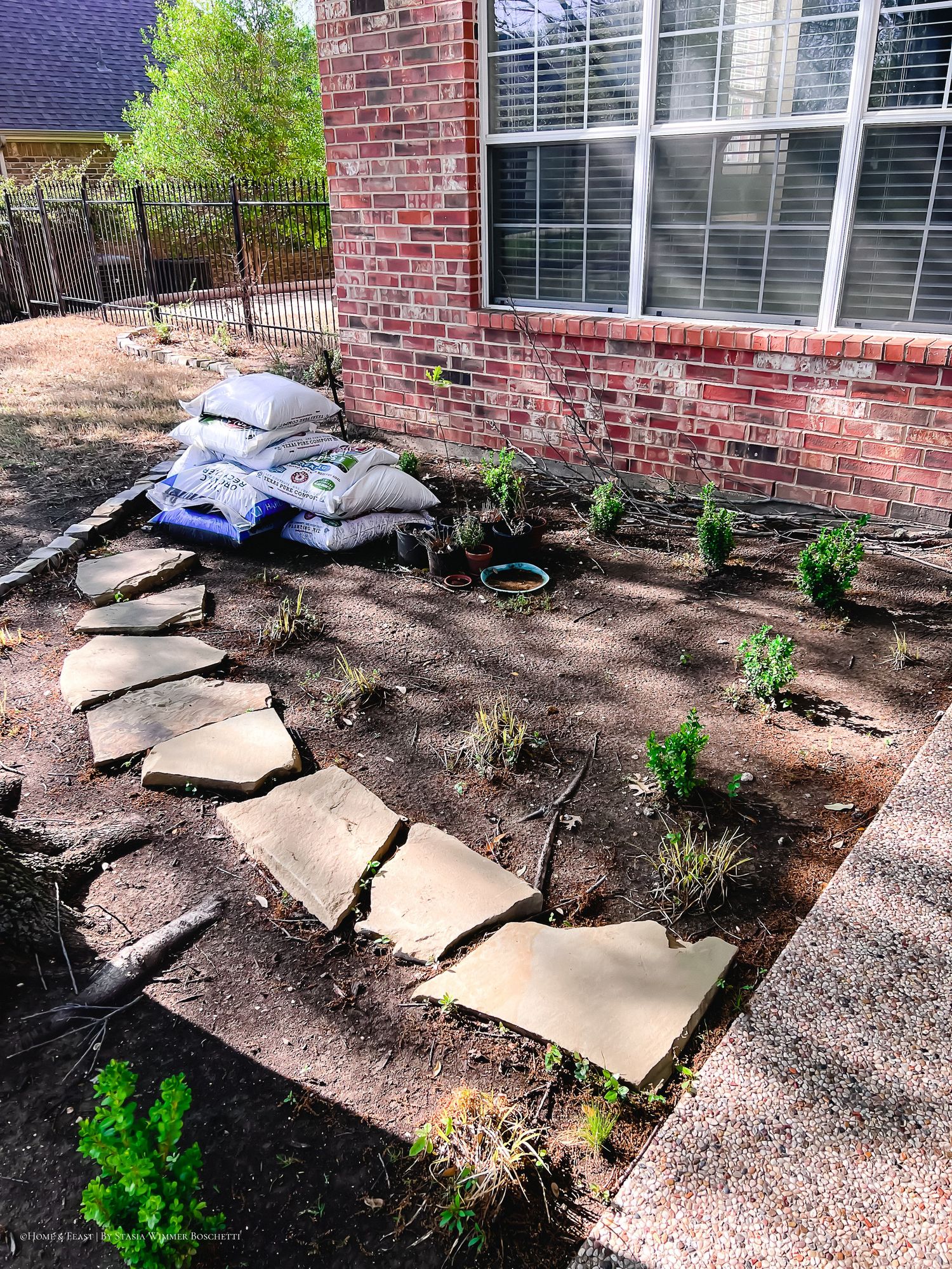 Galvanized raised garden bed with herbs and vegetables growing near a brick wall on a mulched patio.