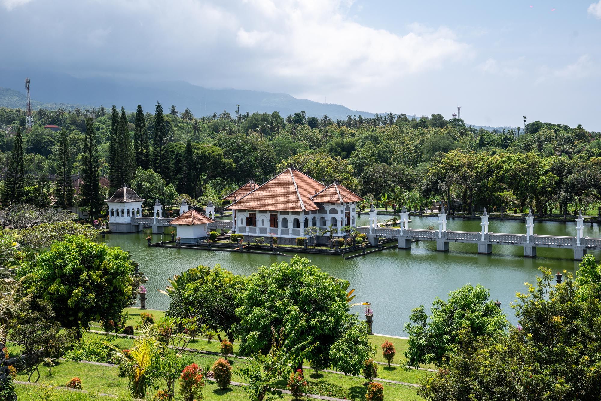 Elegant Balinese water palace surrounded by lush greenery, fountains, and a serene lake with mountain backdrop.