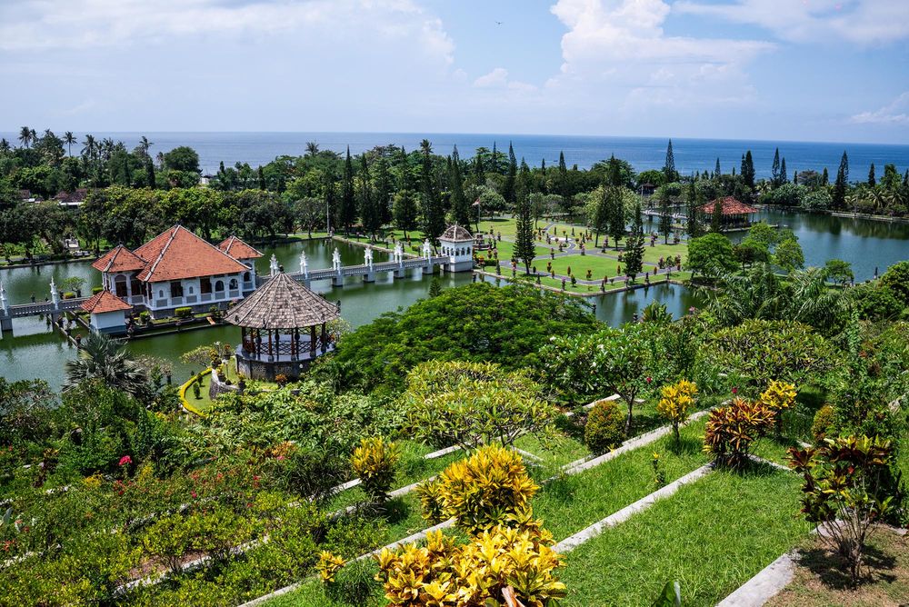 Aerial view of Taman Ujung water palace in Bali with tropical gardens, ponds, and ocean backdrop.