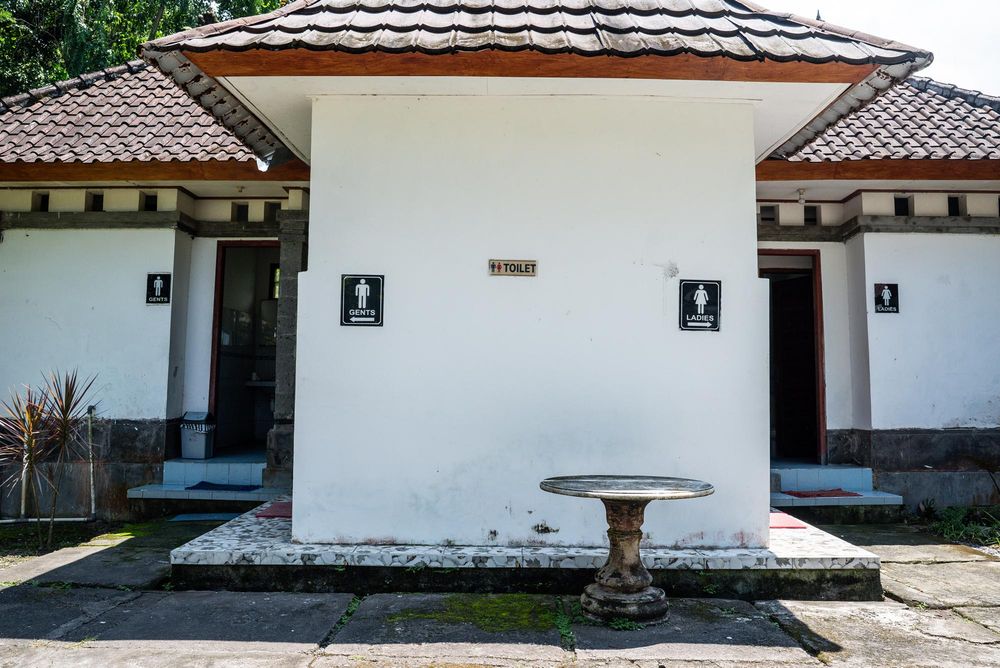 White public restroom building with male and female signs, tiled roof, and stone birdbath outside.