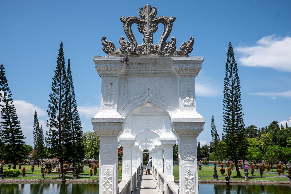White ornate Balinese gate with dragon carvings over a reflective pond at Taman Sari water palace.