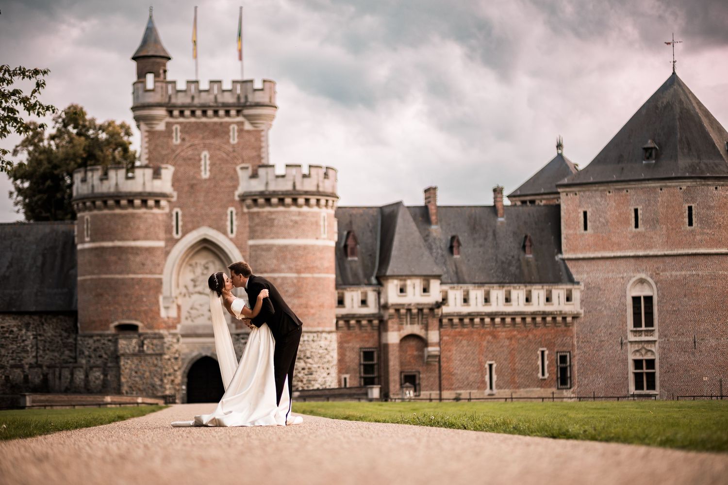 Bride and groom kissing in front of a grand medieval castle on their wedding day.