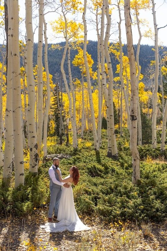 Couple shares a romantic moment among golden aspen trees in a stunning fall forest wedding ceremony.
