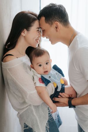 A loving family moment as parents share an intimate moment while holding their baby in casual attire at home溫馨的家庭時光，父母在家中穿著便服抱著寶寶，享受親密的親子時光。