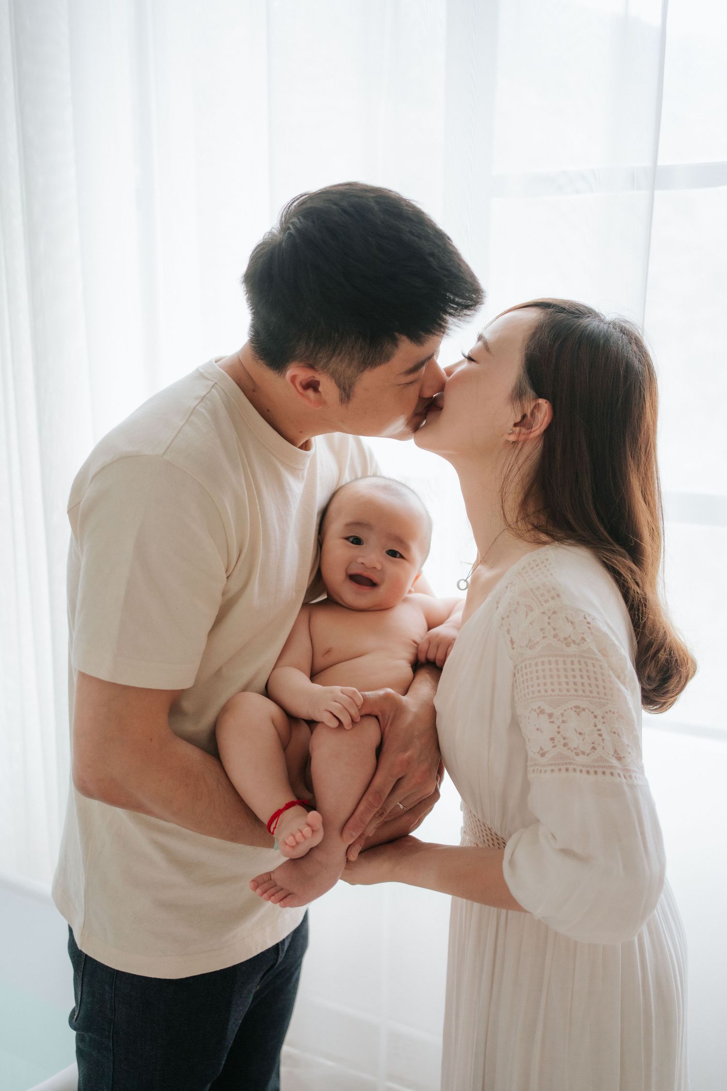 A loving family shares tender moments with their 100 days baby together in a bright white room.在一個明亮的白色房間裡，一個充滿愛的家庭與他們出生100天的寶寶分享溫馨的時刻。