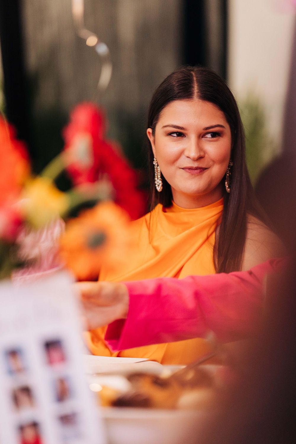 Woman in orange dress smiling at a festive table with colorful flowers and decorations.