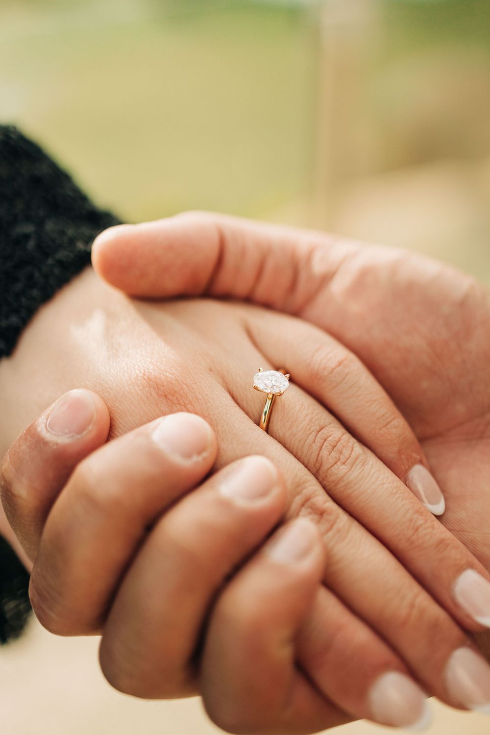 Close-up of two hands holding together with a elegant solitaire diamond engagement ring on the womans finger.