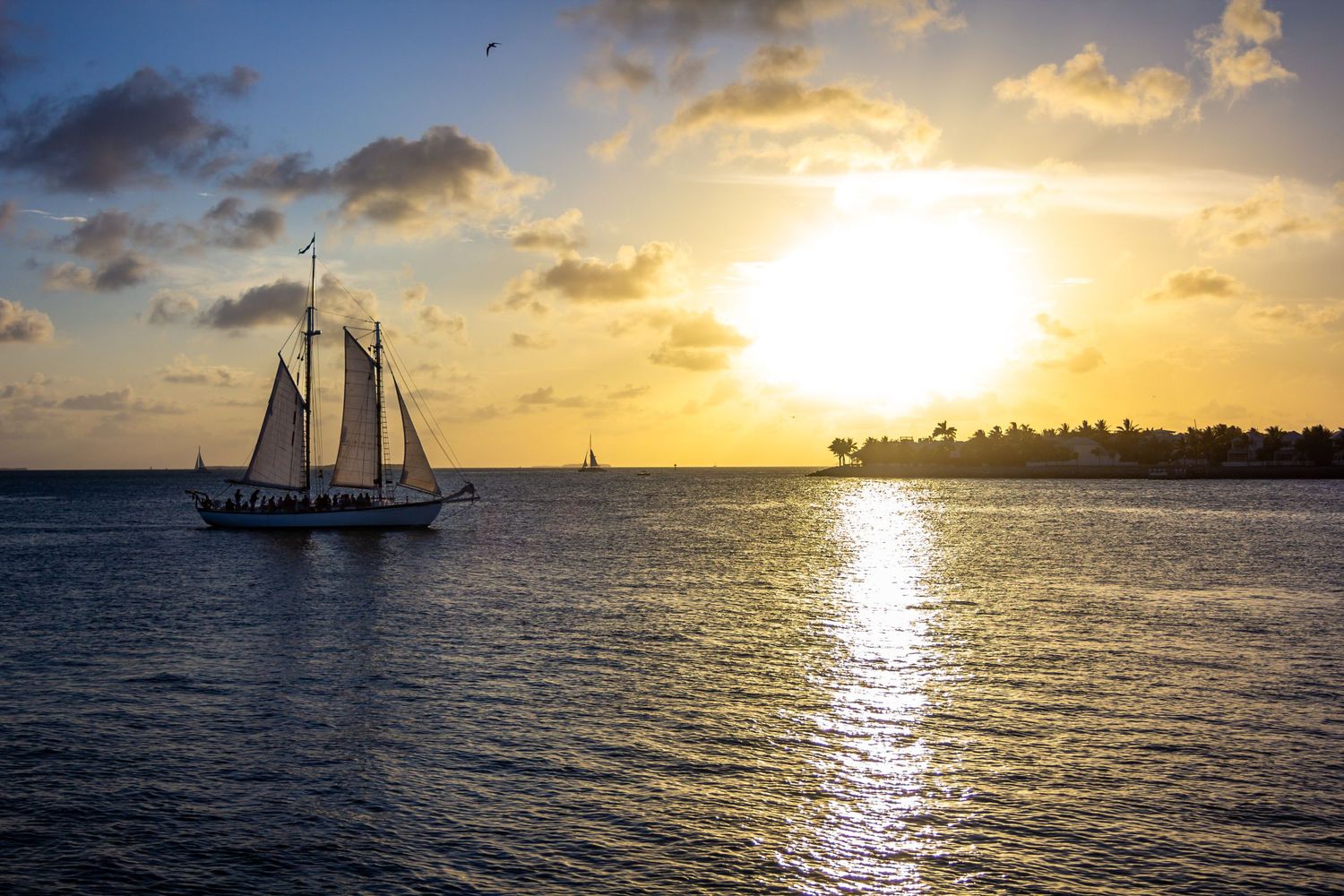Sailboat gliding across calm ocean waters during a stunning golden sunset near Mallory Square