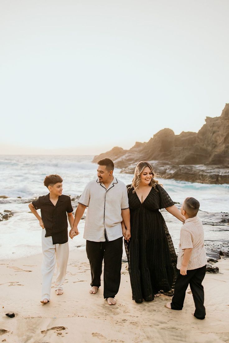 Family of four walking on a sandy beach at sunset, parents holding hands with two boys in coordinated black and white outfits.