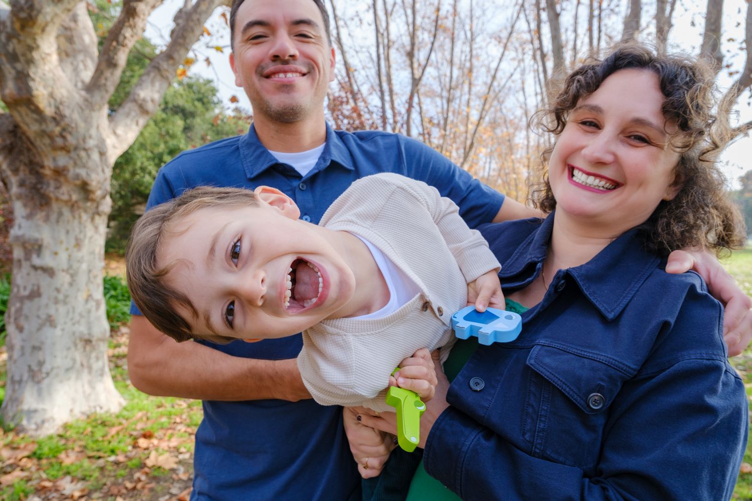 Happy family with two parents holding their laughing young child outdoors in a park during autumn.