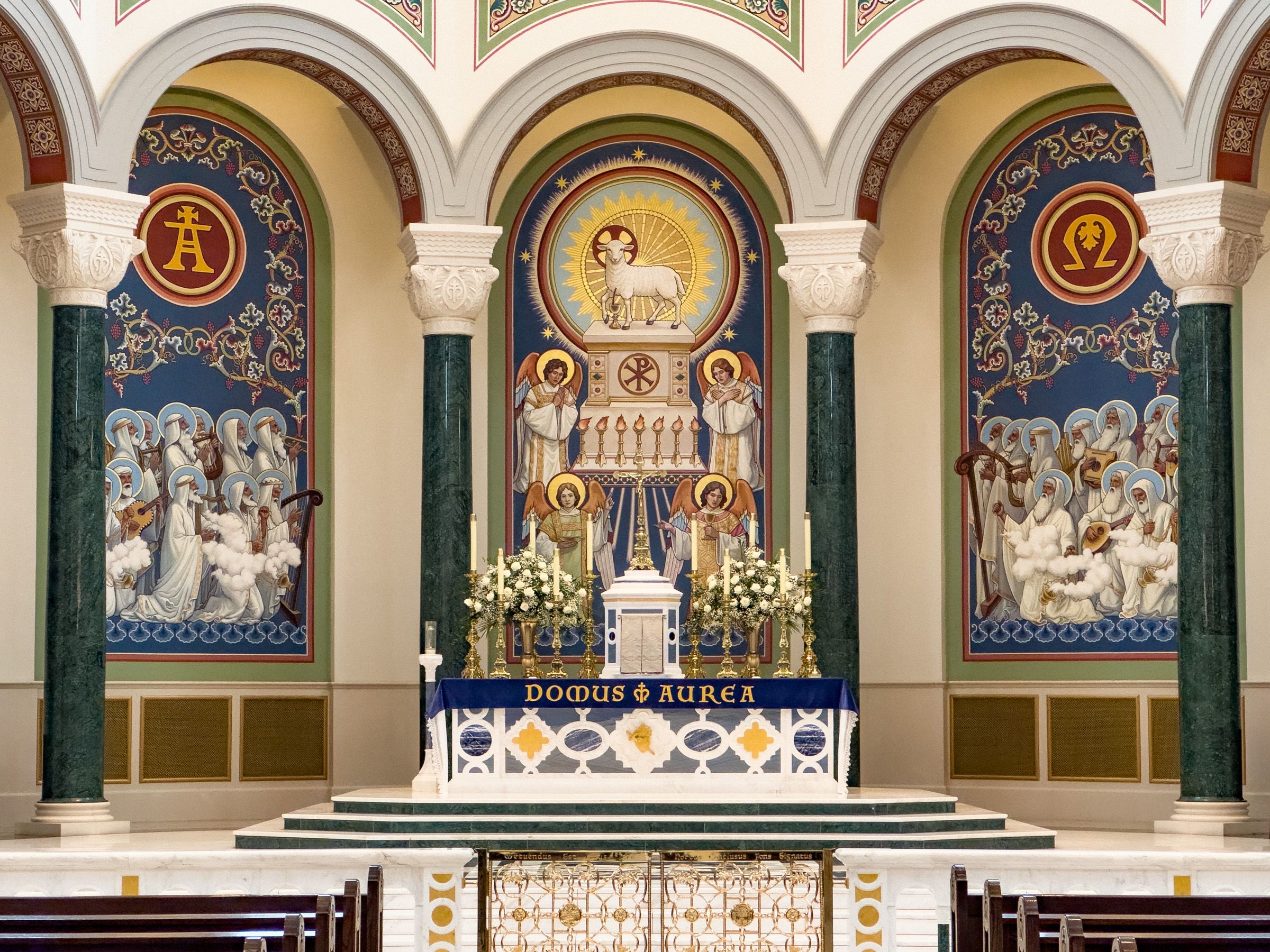 Ornate Catholic church altar with golden mosaics, Alpha and Omega symbols, and colorful Byzantine-style religious artwork.