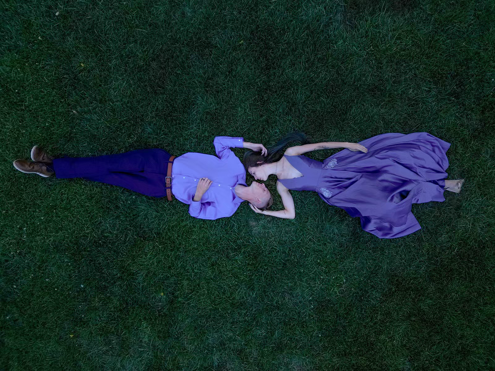 Aerial view of two people in purple outfits lying on lush green grass, creating a artistic overhead portrait.