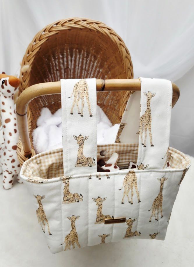 White quilted tote bag with giraffe print pattern, displayed with matching burp cloth on a wicker bassinet.