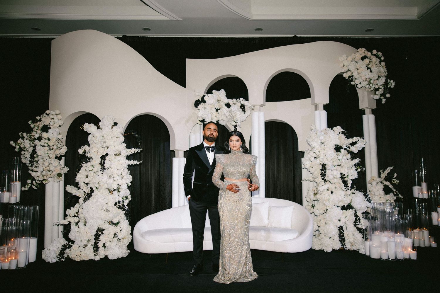 Elegant couple posing before a stunning black and white wedding backdrop with arch decor and white floral arrangements.