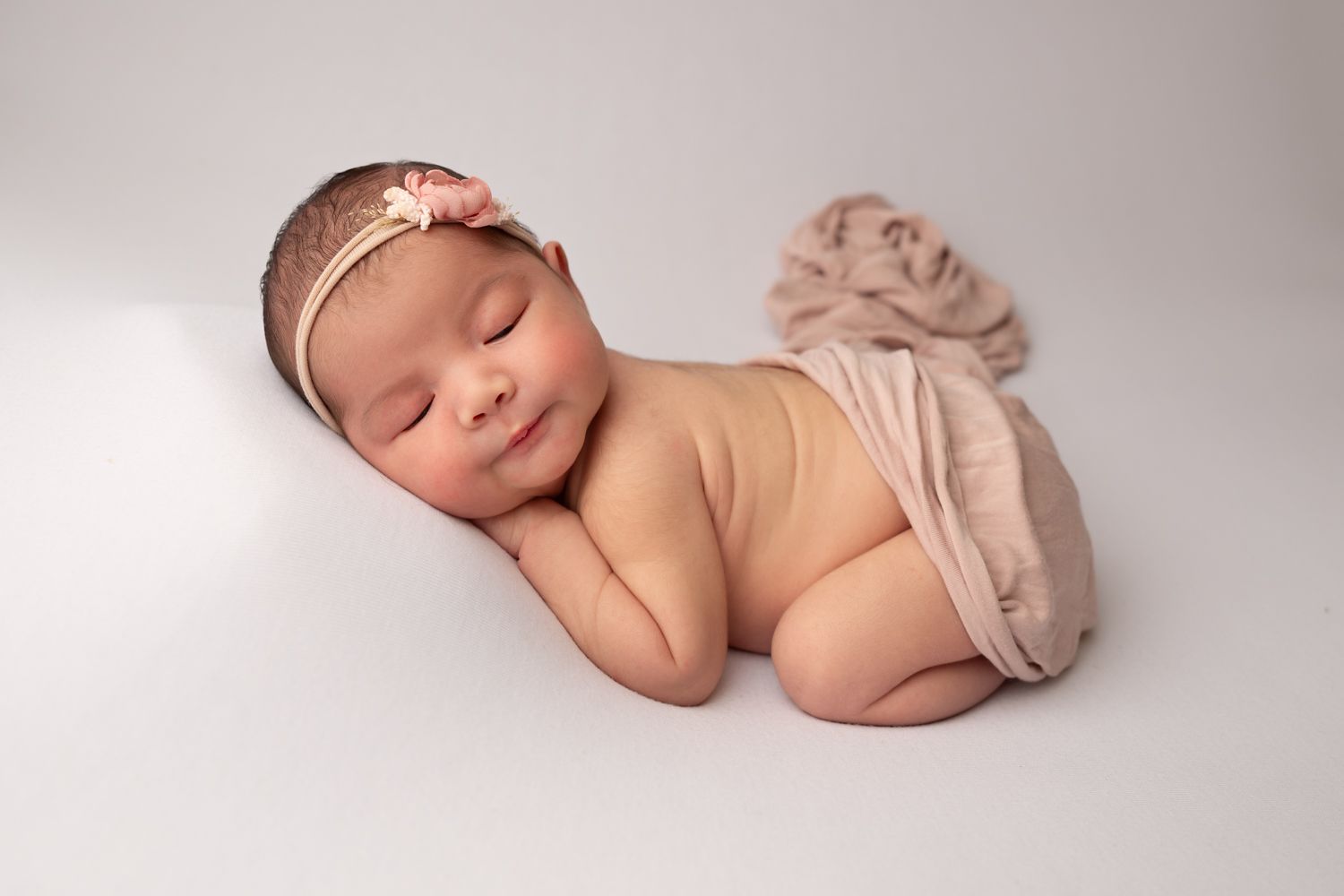 Smiling toddler girl in white dress holds sleeping newborn baby wrapped in blue on a fluffy cream rug.