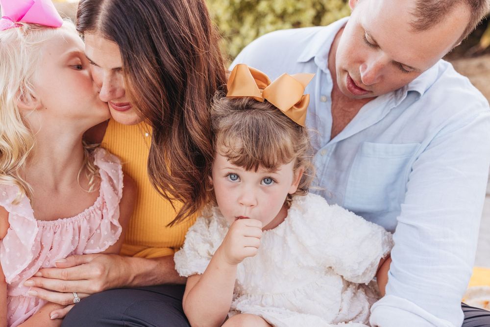Family portrait with two young girls, parents sharing a tender moment outdoors.