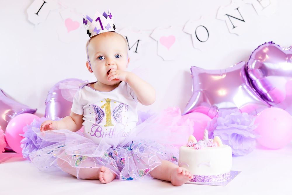 Pink and purple first birthday cake smash setup with tulle dress, crown, and heart balloons.