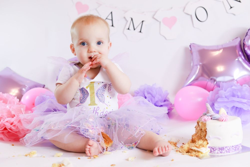 First birthday celebration with cake smash, pink balloons, and purple tulle decor.