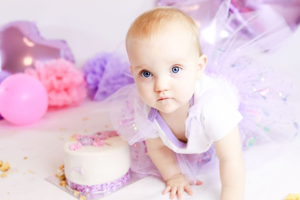 White cake surrounded by pink and purple decorations for first birthday photoshoot.