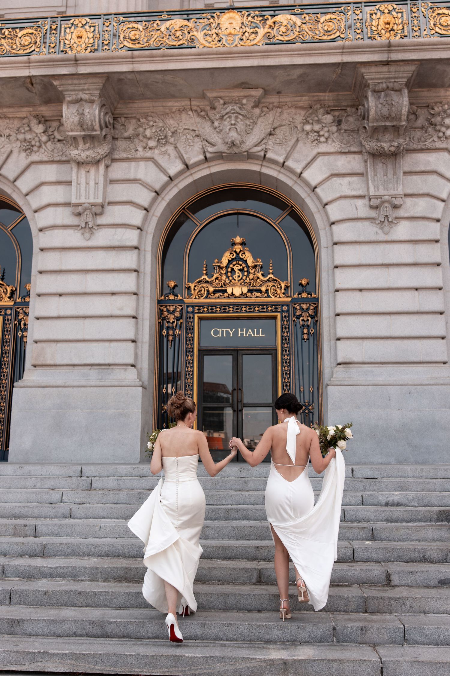 Elegant wedding reception in a grand hall with navy blue tablecloths, gold chairs, floral centerpieces, and a ornate staircase.
