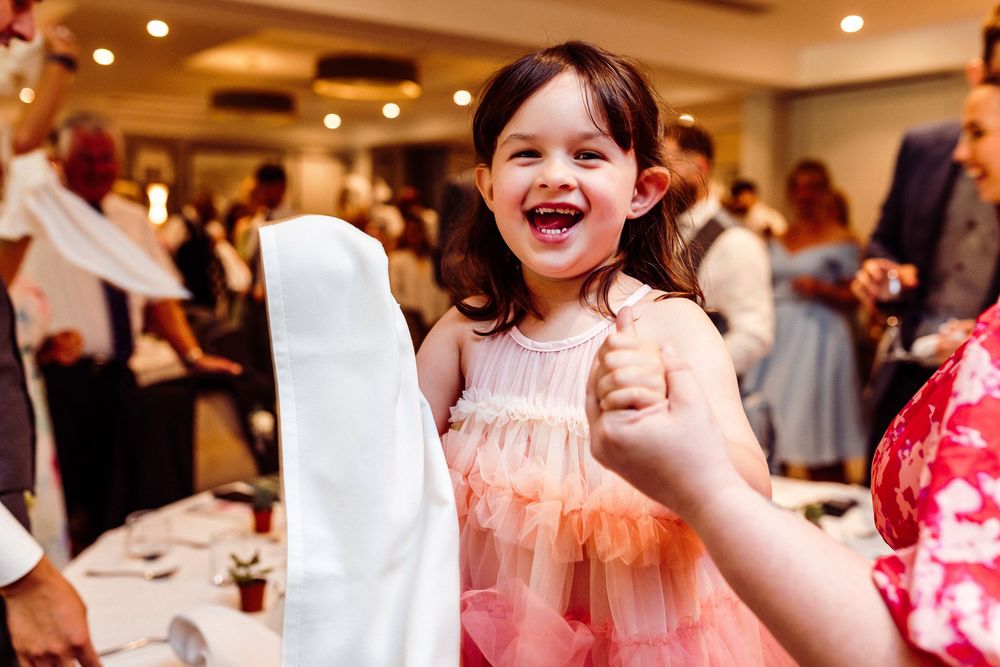 Joyful little girl in pink tutu dress laughing and pumping fist at elegant wedding reception venue.