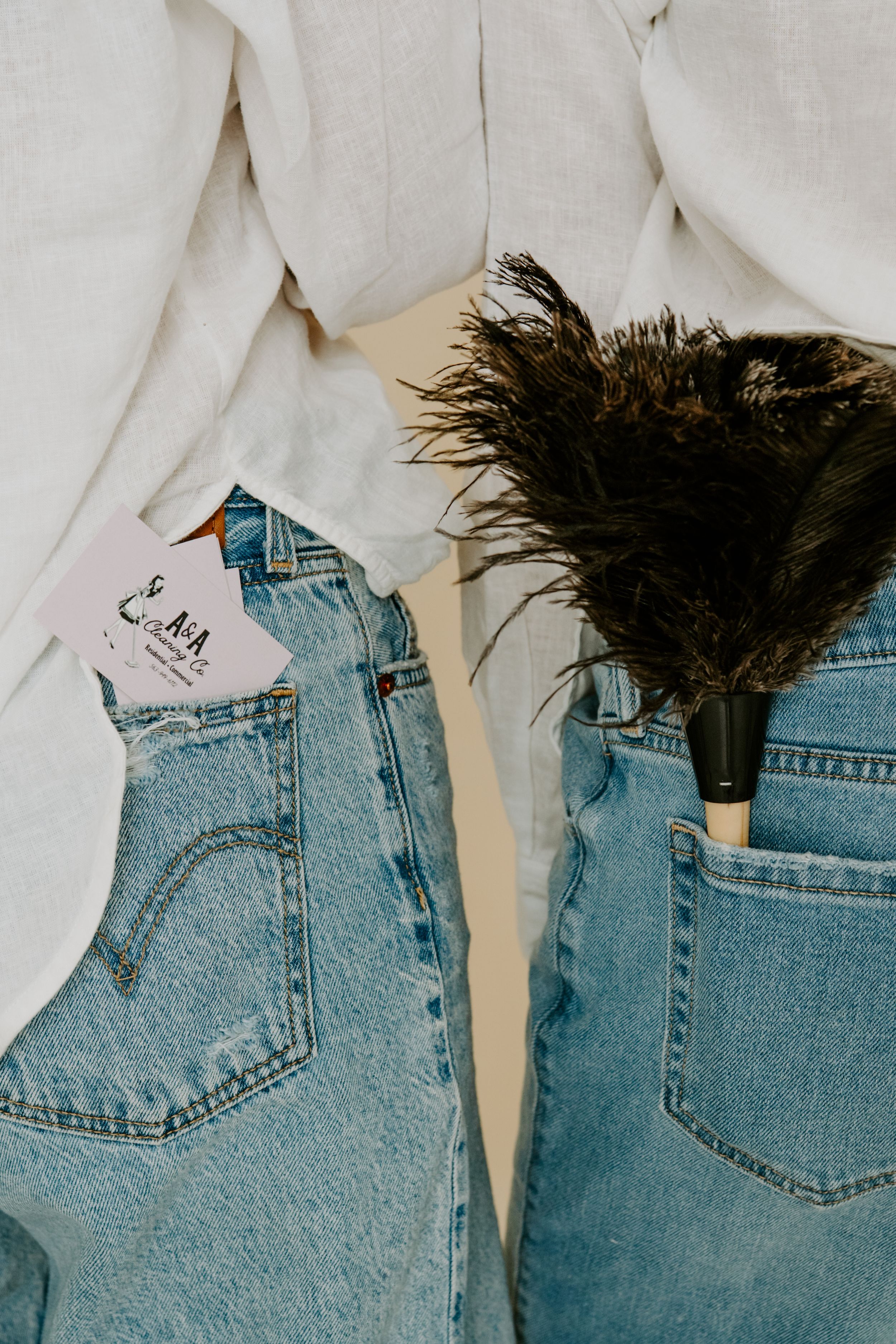 Two people in light wash Levi's jeans with white shirts, one holding a business card and other a feather duster.